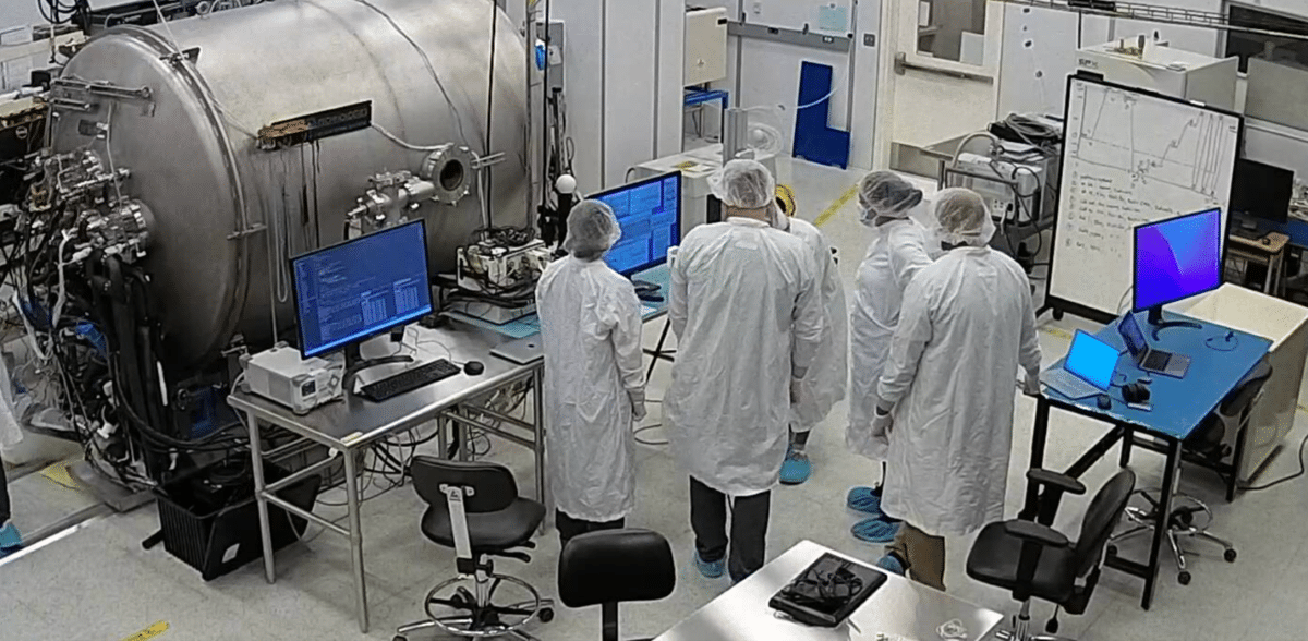 People wearing lab coats, head coverings, and masks in the Thermal Vacuum Testing Facility at ASU.
