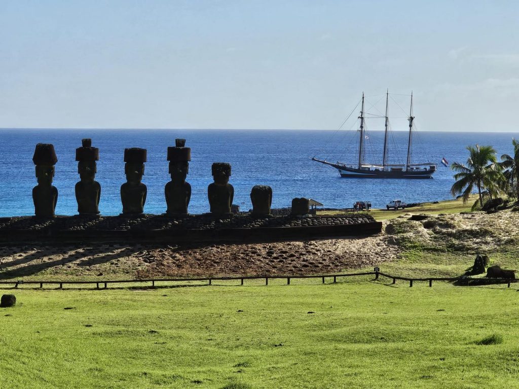 ancient Polynesian statues on the coast of Rapa Nui with a tall ship in the background
