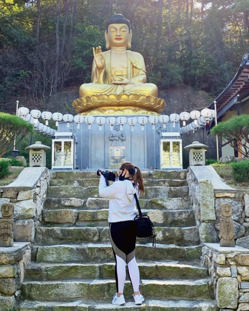 Hailey Lopez taking a photo of a large Buddha statue in South Korea