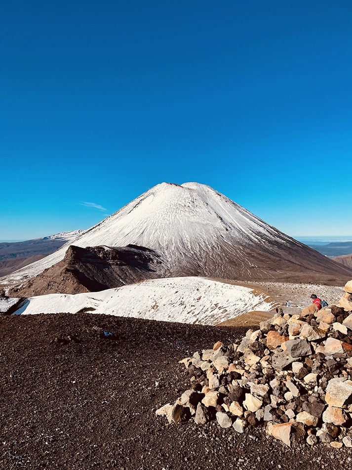 Blue sky and a snow-covered mountain with a large rock cairn.