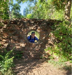 Sarah Negovan looking through a hole in a wall on the West Fork Trail.