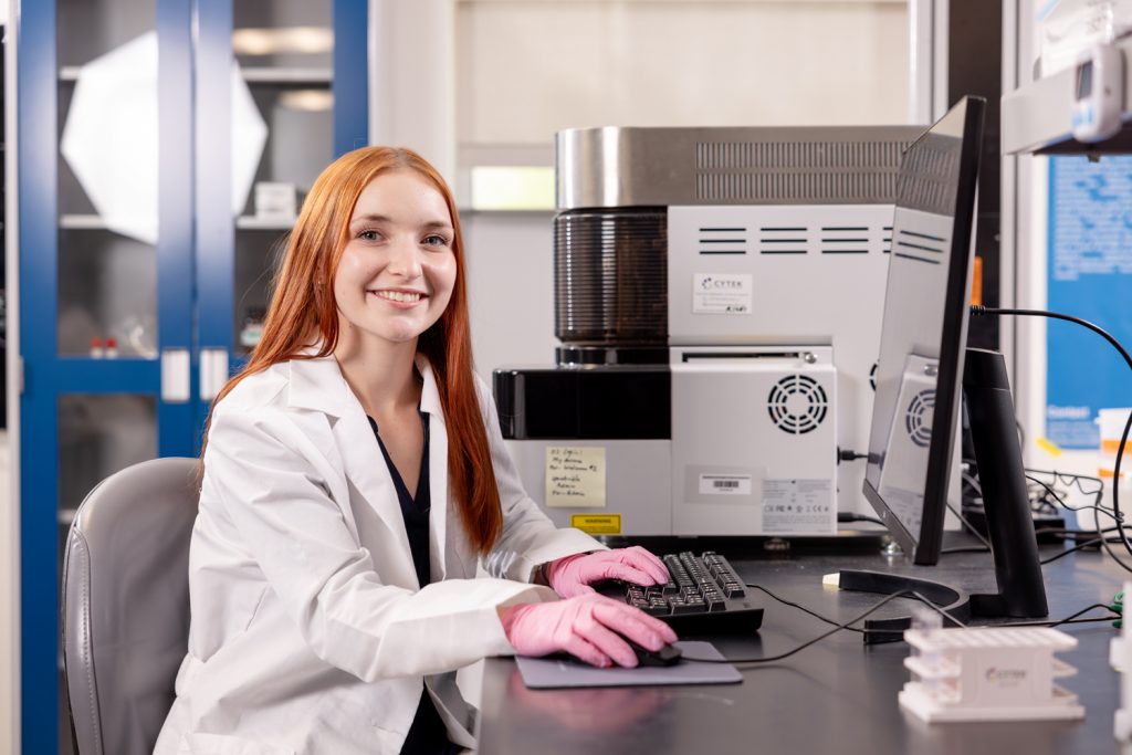 Sophia Justice wearing a lab coat and sitting at a computer