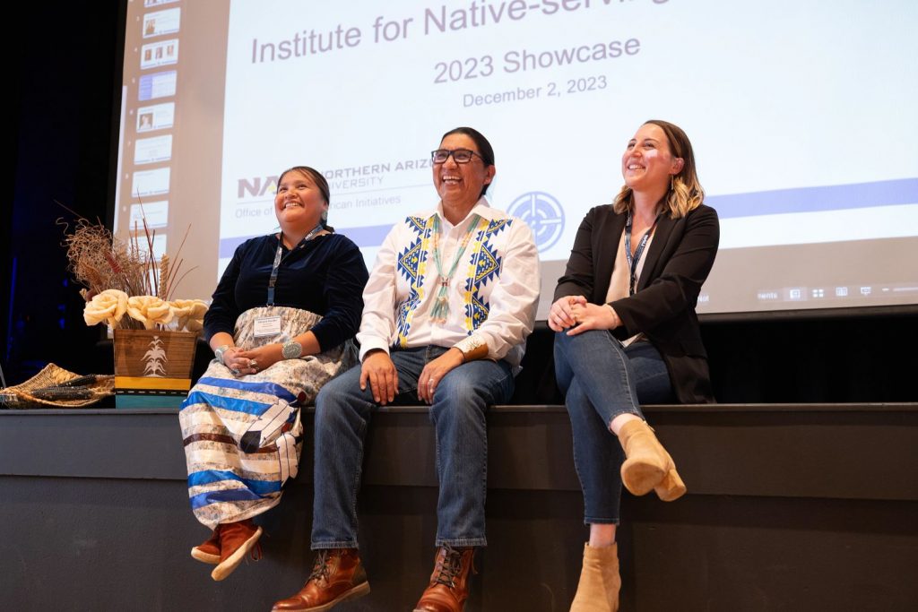 Darold Joseph sitting between two women on a stage at the Institute for Native-Serving Educators showcase in 2023