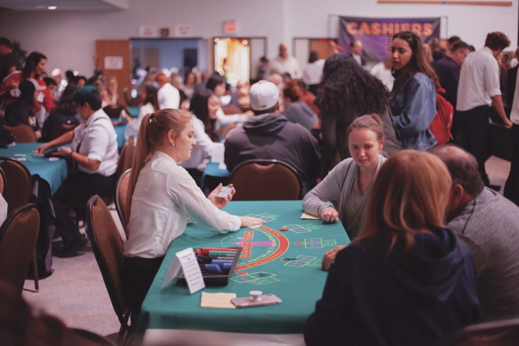 student wearing a white shirt and black pants dealing at a poker table