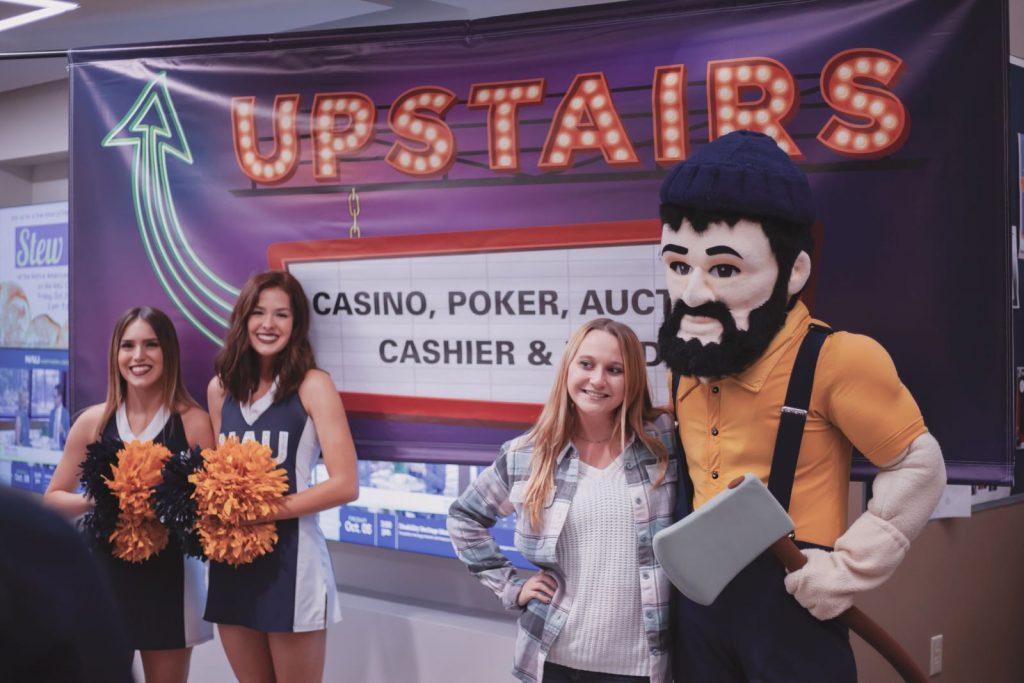 cheerleaders, a student and Louie posing in front of a Casino Night sign in the du Bois Center at NAU