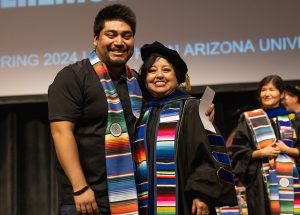 A student in a Hispanic graduation stole hugs a professor in regalia.