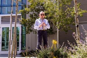 Carlos Nakai playing flute in with native plants at Nakai Plaza in foreground