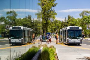 students stepping onto a shuttle bus next to a reflective glass building