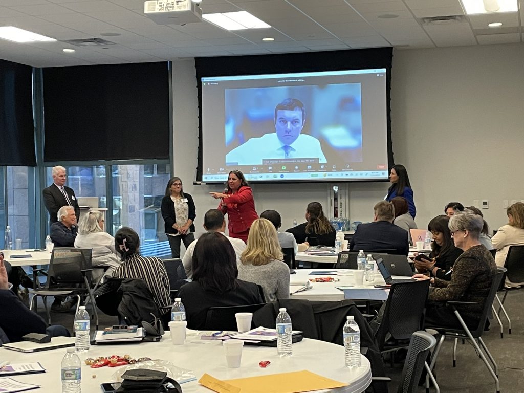 people sitting at conference tables turned toward a woman speaking at the front of the room