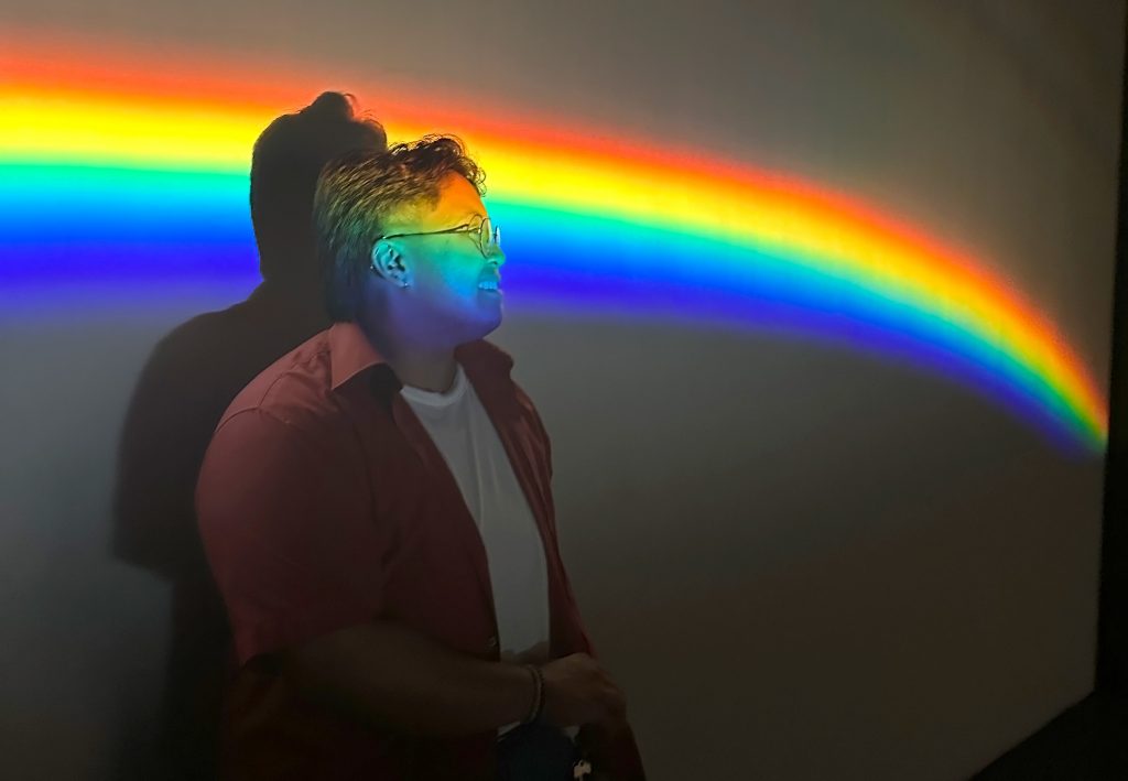 Jaden Blake L. Reyes posing in front of a projected rainbow