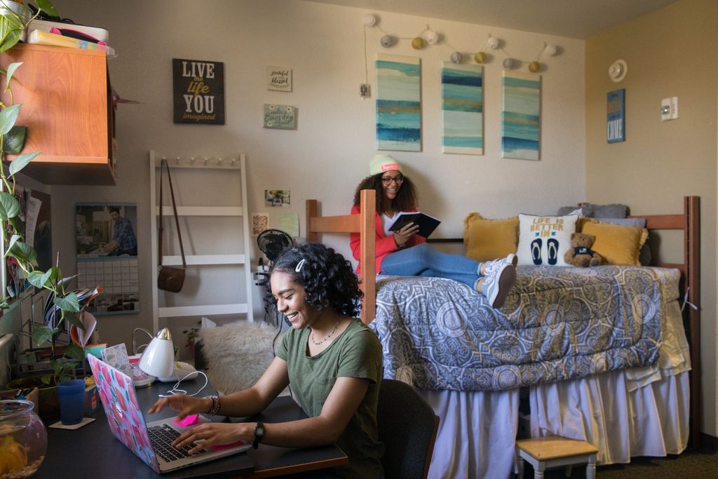 Two students in a dorm room with a lofted bed