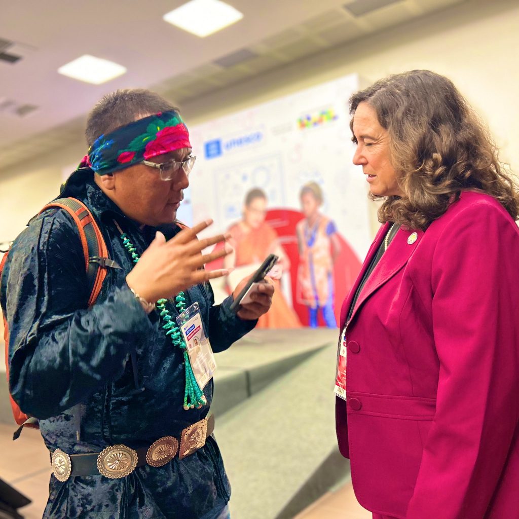 Ryan Chee wearing traditional Diné clothing and talking to Deputy Secretary of Education Cindy Marten