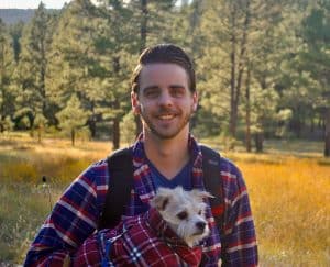 Graduate Cody Rieffer in flannel in the forest holding a small white dog