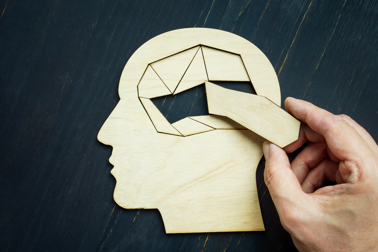 hand putting a missing piece inside a wooden puzzle in the shape of a brain