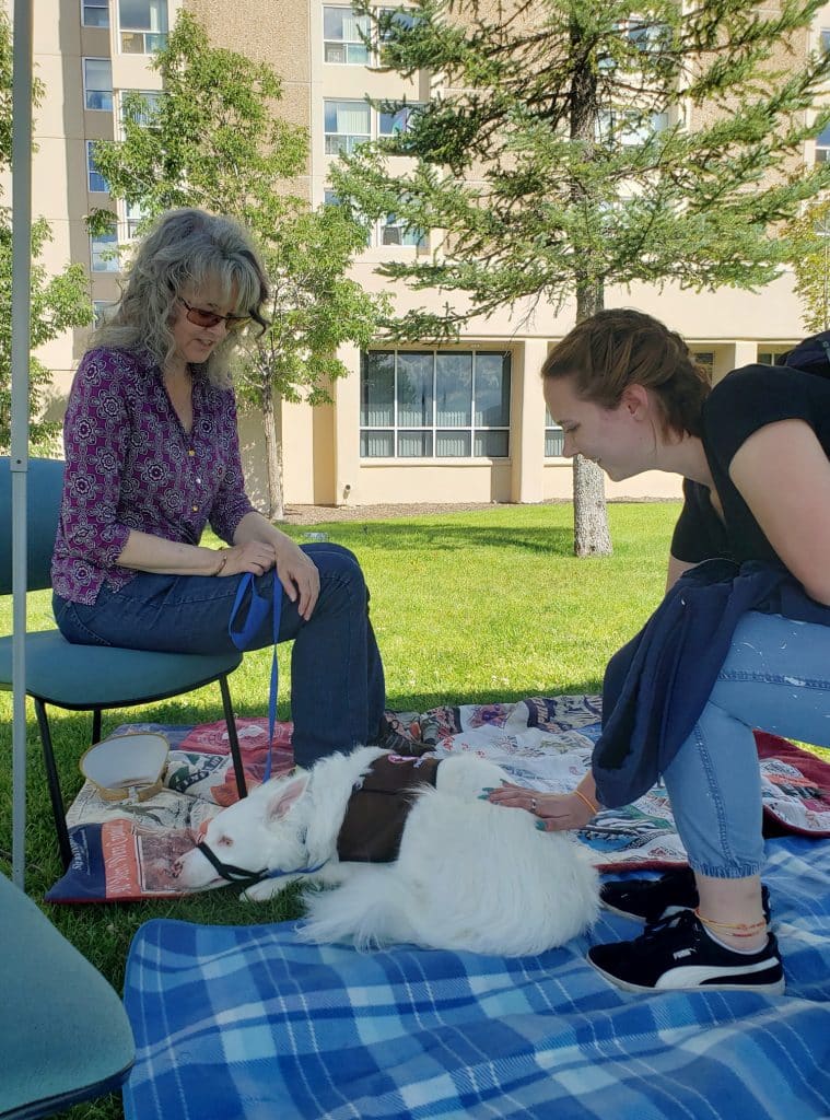 woman looking on as a student pets her fluffy white dog