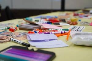 Table filled with markers of different colors, paper and glue sticks.