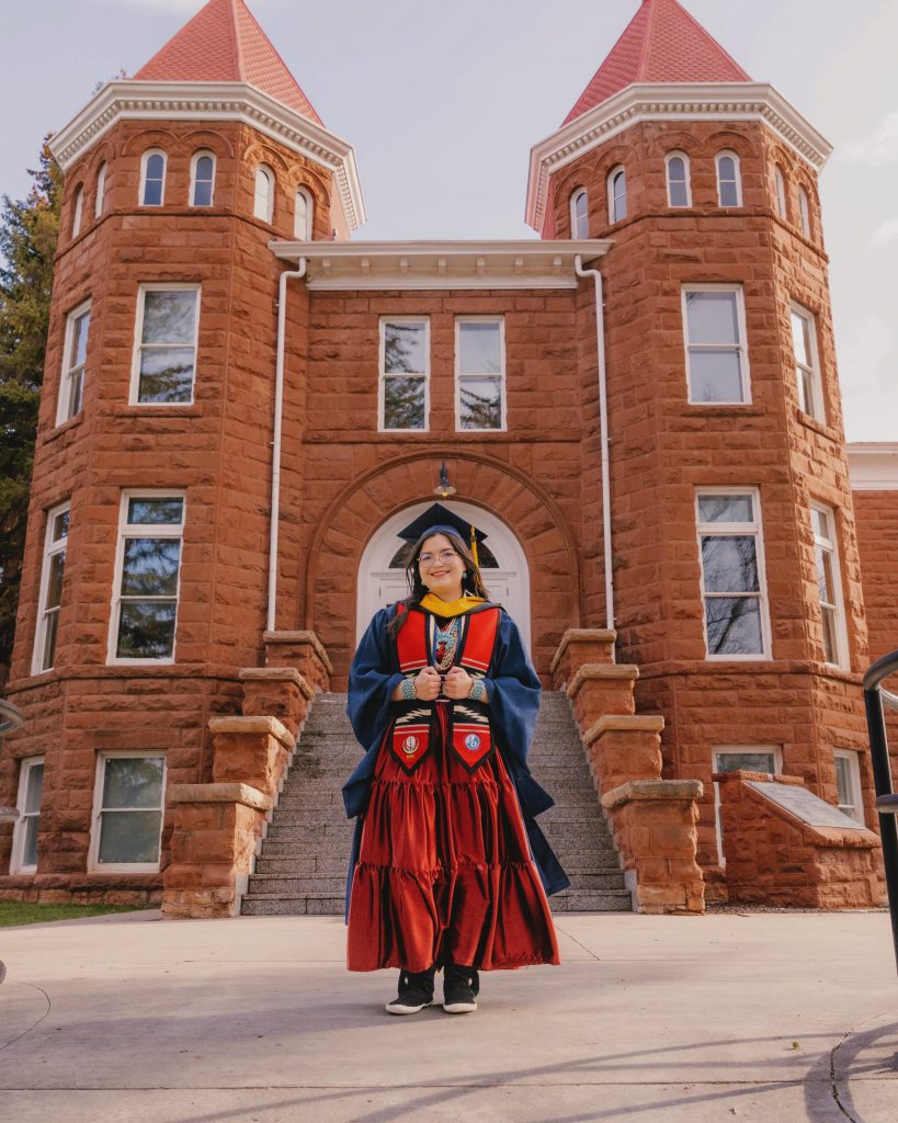Kaylin McLiverty dressed in graduation regalia in front of Old Main