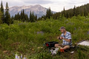 Richardson preparing a camera for the PhenoCam study. He is sitting in the middle of a meadow.