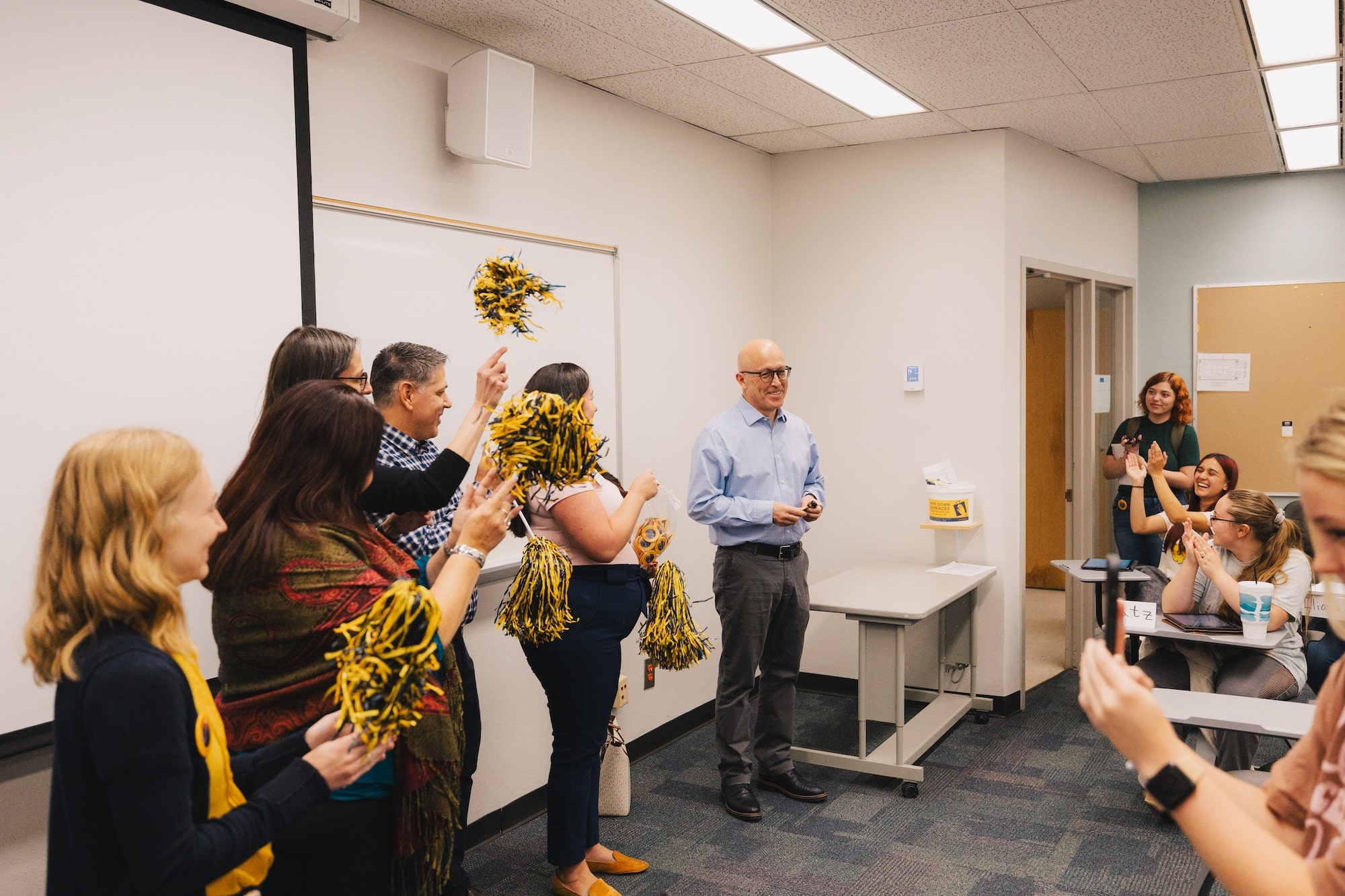 Alex Alvarez stands at the front of his violent crime classroom while a group of his colleagues and student organization leaders cheer and clap around him.