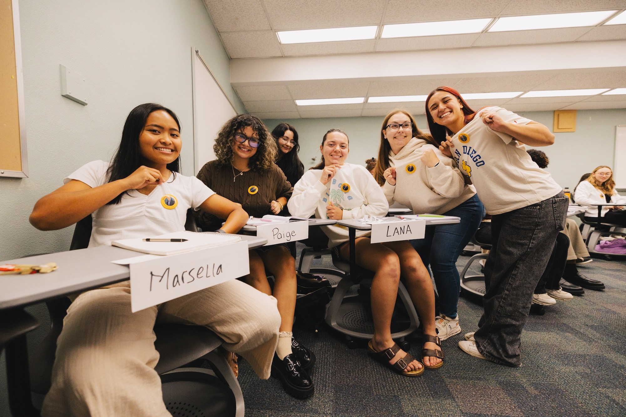 Six of Alex Alvarez students pose holding customized Homecoming dedicatee buttons with Alvarez's face on them.