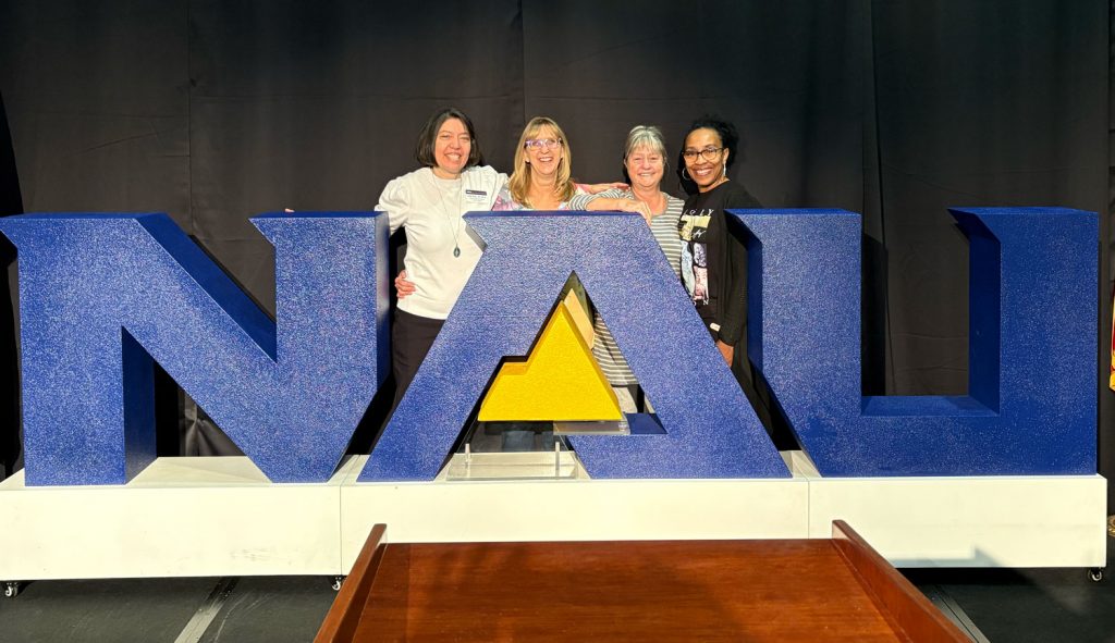 Adrien Gupton posing with colleagues behind a large NAU logo