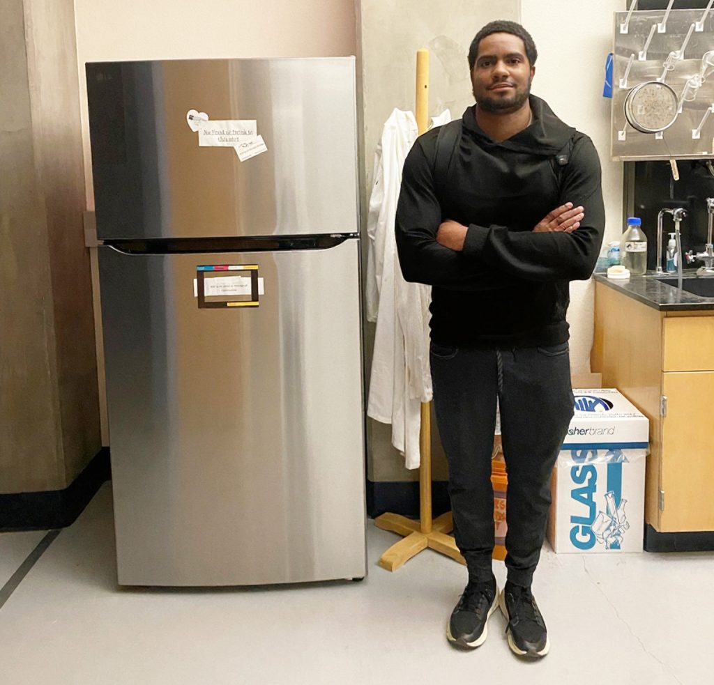 Trey Cooper posing next to a brand new refrigerator in the Science Lab