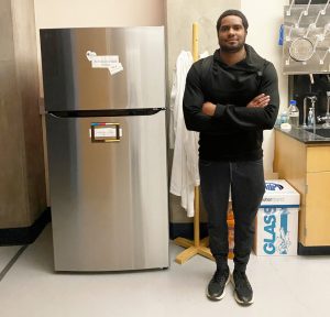 Trey Cooper posing next to a brand new refrigerator in the Science Lab