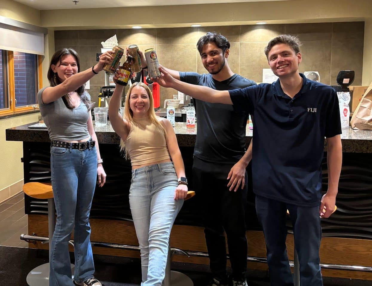 Four NAU Brew Club members toast with canned beverages in the Hotel and Restaurant Management building.