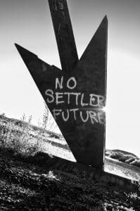 Black and white picture of arrow with graffiti that reads No Settler Future