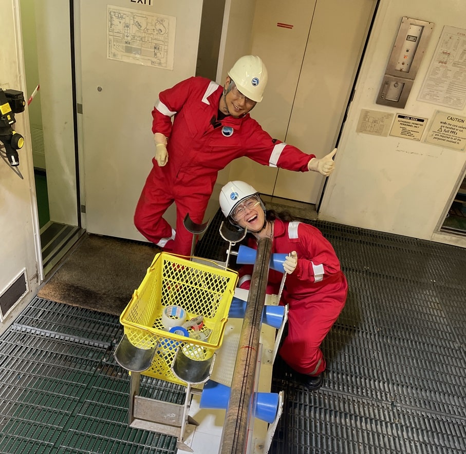 Christine Regalla in PPE with one other researcher posing in front of a sediment funneling machine