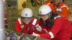 Christine Regalla and another researcher in orange PPE and helmets looking at a sediment sample
