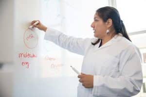 Naomi Lee drawing on a whiteboard while wearing a white lab coat