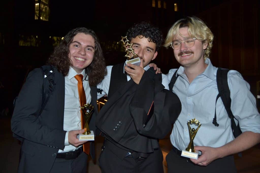 Three male members of Mock Trial Club pose with individual competition trophies.