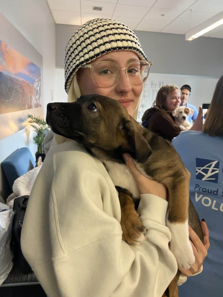 A student in a black-and-white knitted hat holds a brown puppy in her arms.