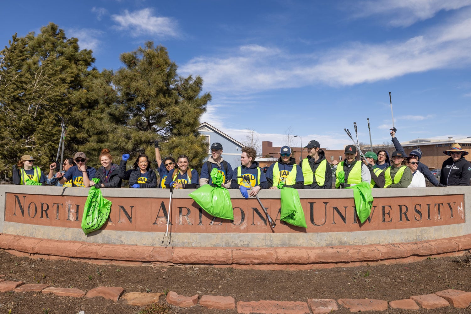 Group of employees holding trash bags in front of a Northern Arizona University sign