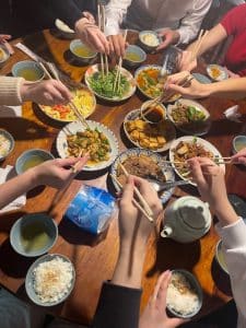 Hands with chopsticks on top of a wide variety of dishes