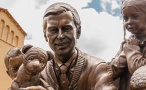 Bonze statue of Mister Rogers. He is holding a dog and kids are around him.