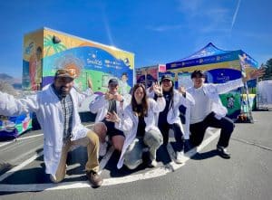 Six SparCQS volunteers in white lab coats pose in front of the project's new California-themed trailer.