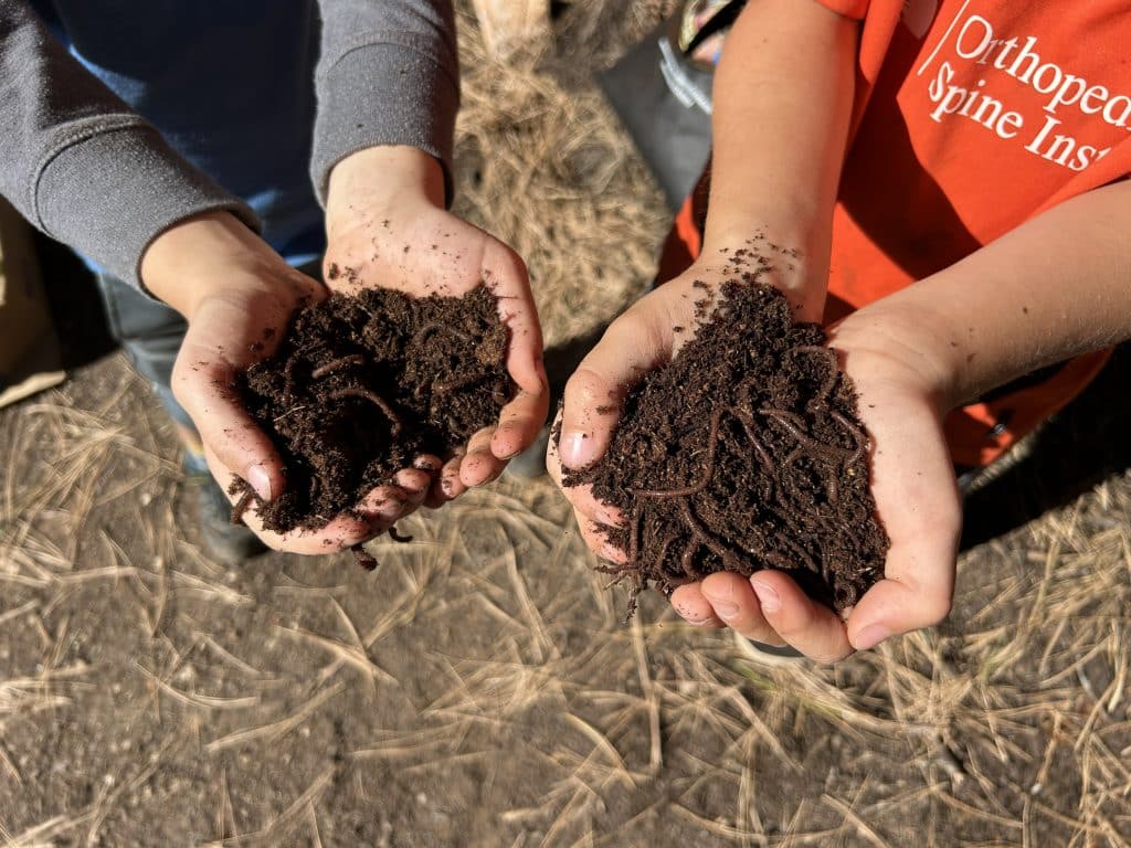 Two pairs of hands holding soil with worms inside of it