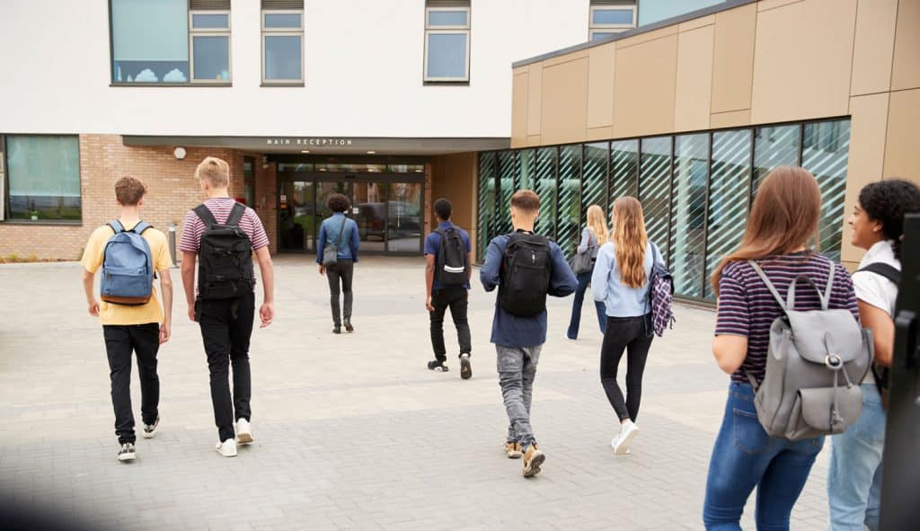 Teenagers with backpacks walking toward a school entrance