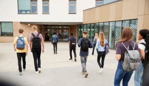 Teenagers with backpacks walking toward a school entrance