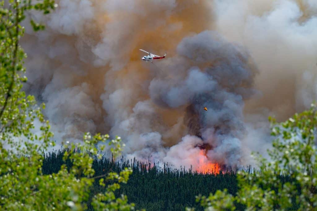 Emergency helicopter flying above a forest fire and billowing smoke