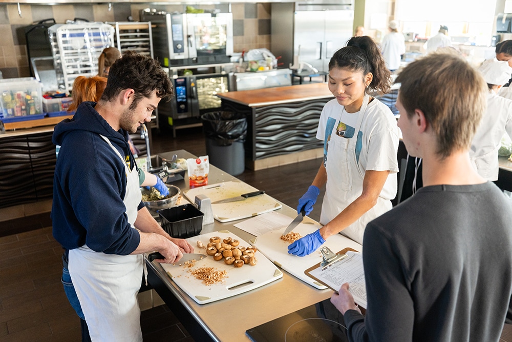 Los estudiantes preparan champiñones mientras otro estudiante observa su proceso.