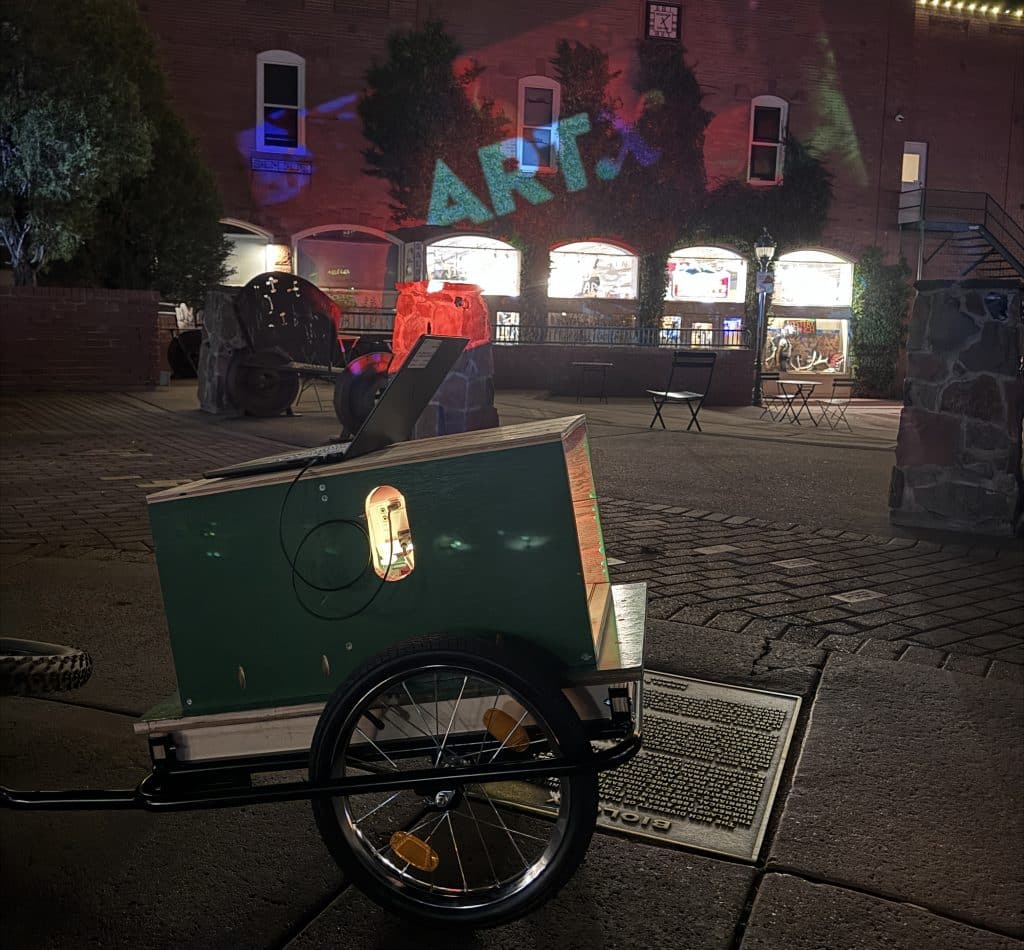 Projector on wheels projecting the word 'ART' on a building.