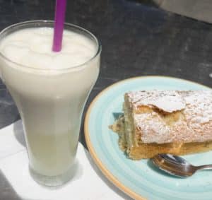 Horchata drink in a large cup next to a cake on top of a blue palate with a spoon