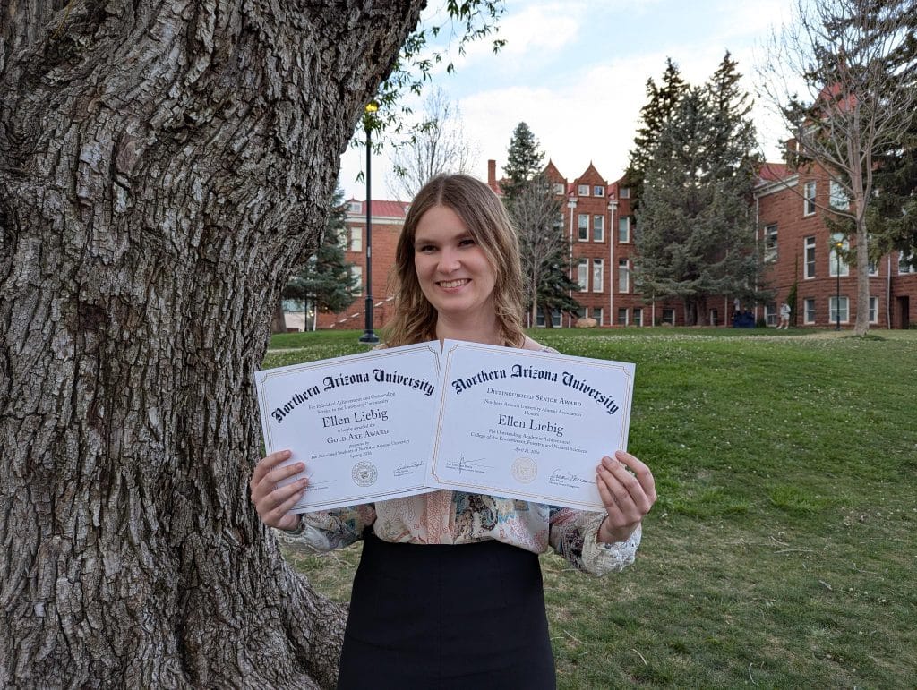Ellen Liebig holding paper Distinguished Senior and Gold Axe awards on the NAU campus