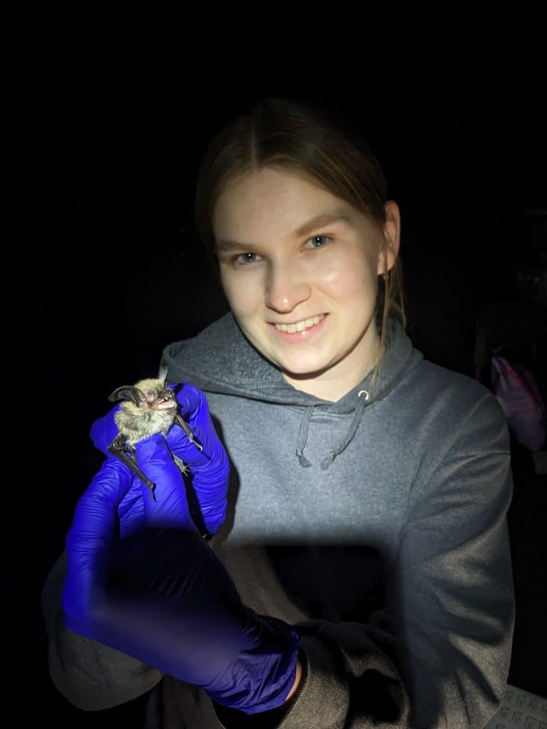 Ellen Liebig holding a bat inside a dark cave