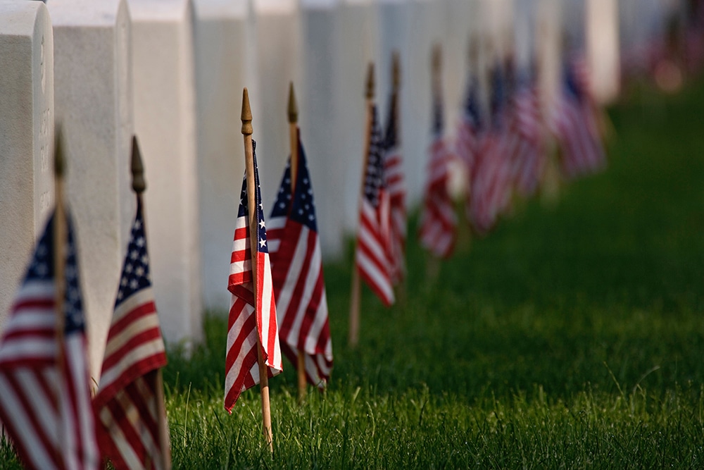 A row of American flags in front of a white fence.